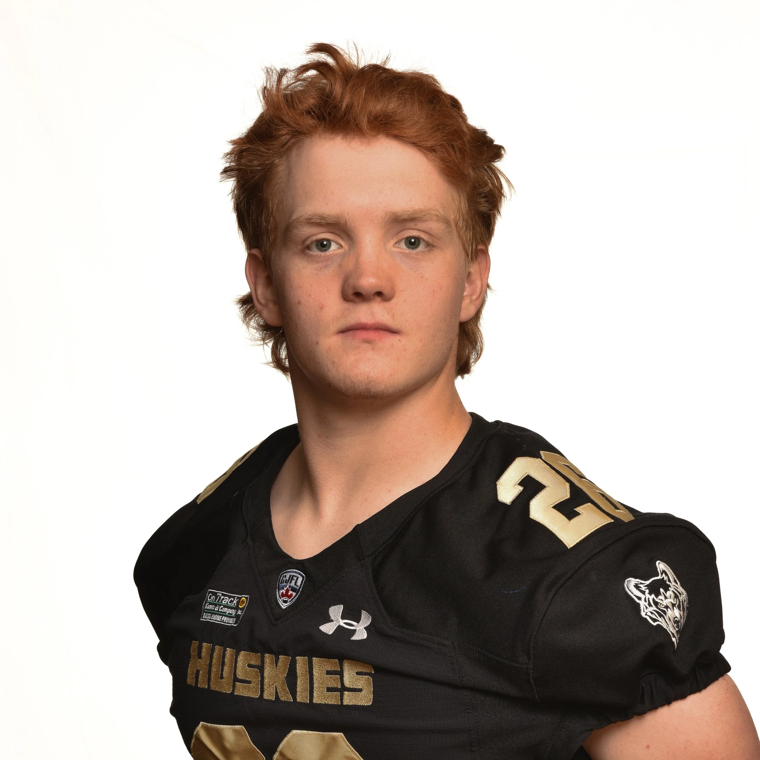 Young man wearing a black sports jersey with 'Huskies' written on it, standing against a plain background.