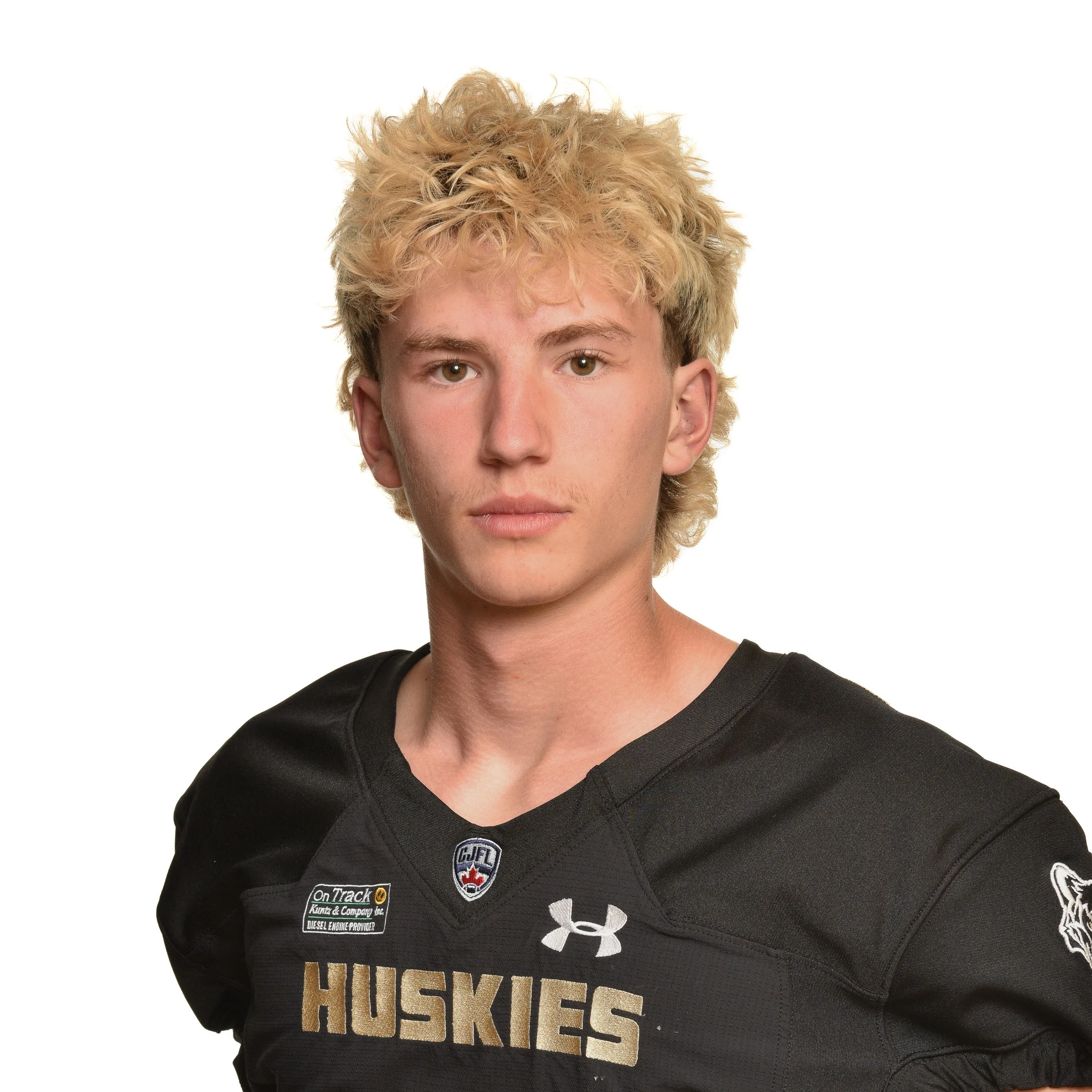 A young male football player with curly brown hair wearing a black and gold Huskies football jersey.