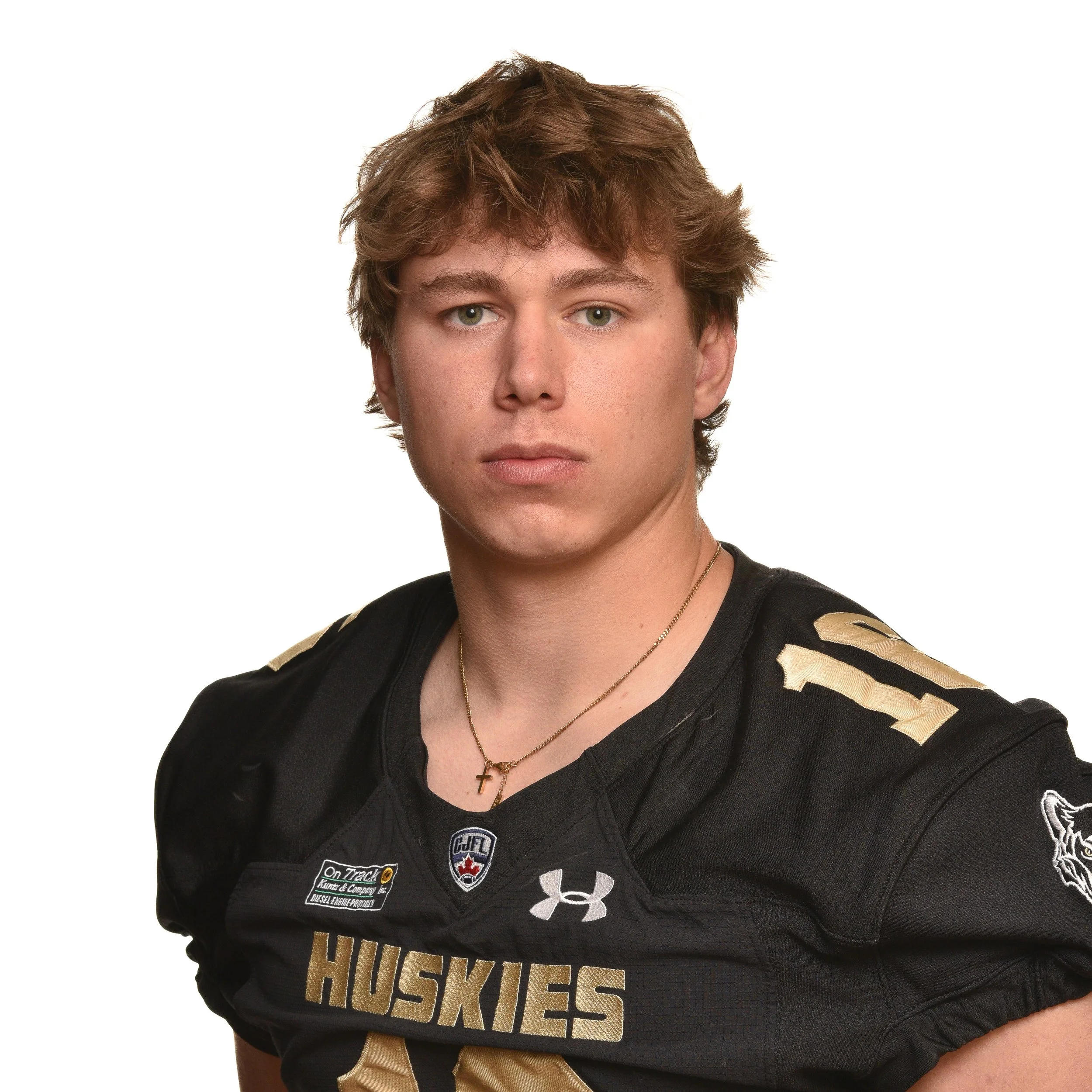 A young man with light brown hair wearing a black football jersey with 'Huskies' written on it and various patches and logos.