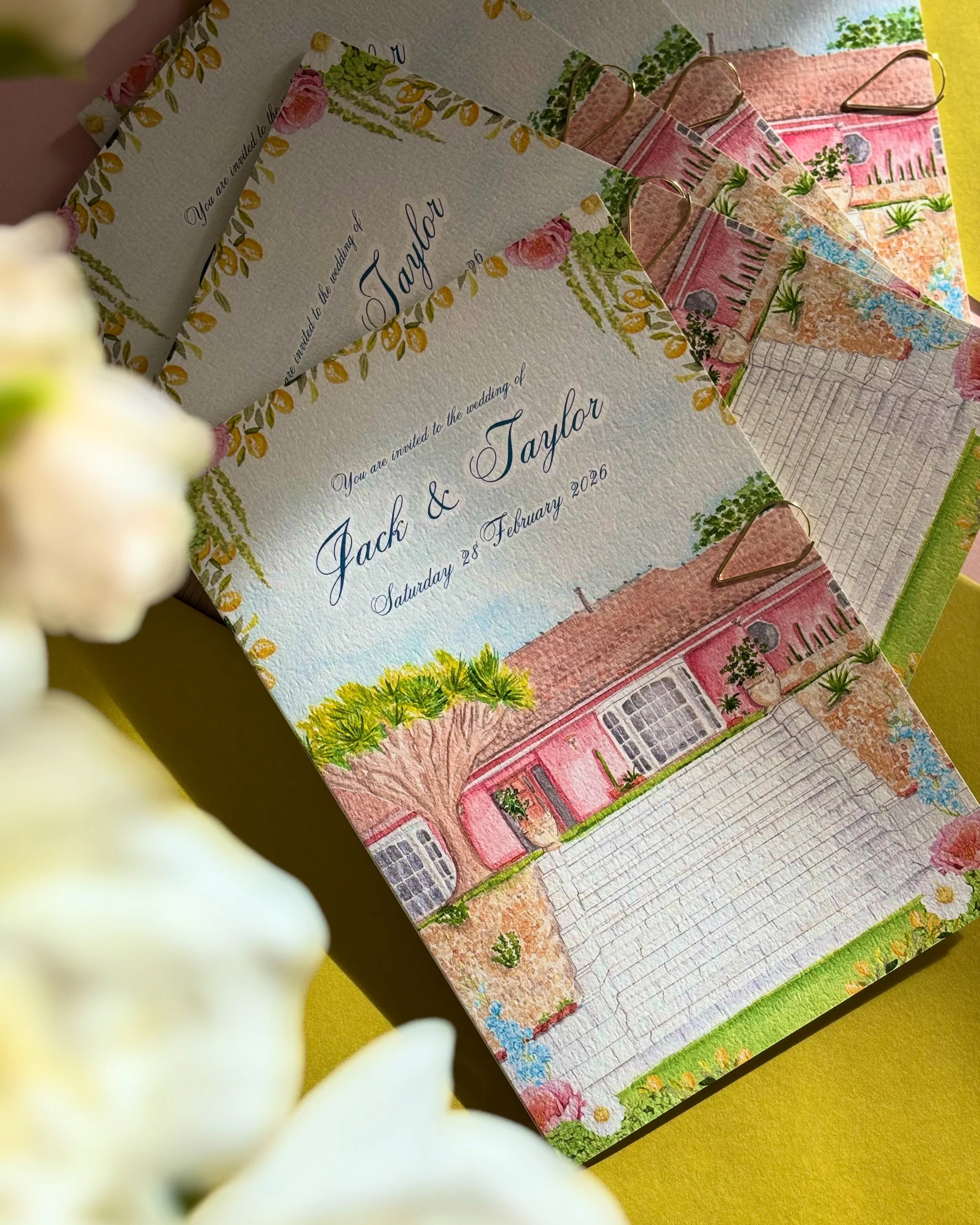 Wedding invitation card featuring an illustration of a pink house with a large tree and potted plants, with floral border and cursive text inviting Jack and Taylor to a wedding on Saturday, February 28, 2026.