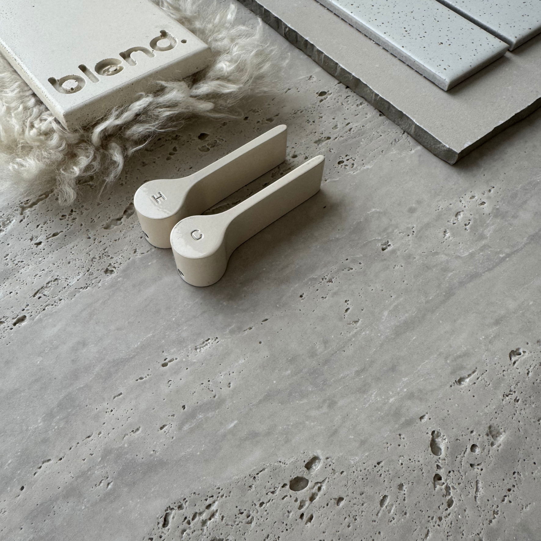 Travertine Classico Stone grey porcelain tile styled with off-white bathroom accessories, textured fabric, tile samples and neutral materials highlighting its travertine-look surface.