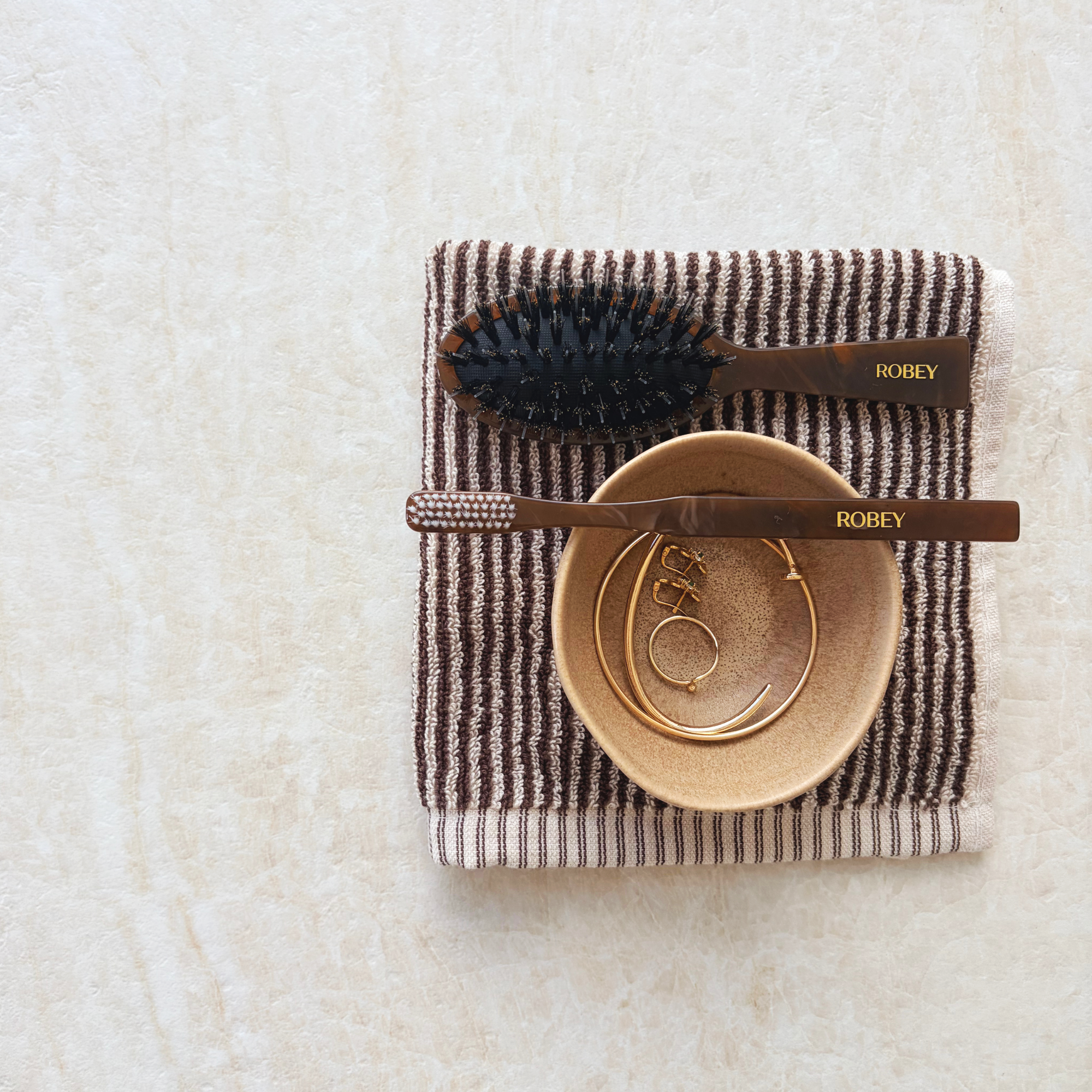 Taj Mahal quartzite-look porcelain tile styled with a burgundy-striped towel, wooden brushes and a small ceramic bowl.