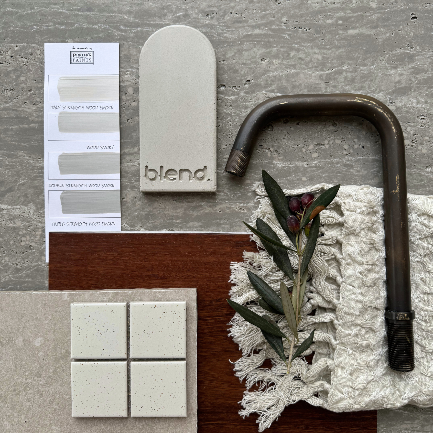 Travertine Classico Ash porcelain tile material flatlay featuring dark metallic tapware, timber samples, fabric swatches, mosaic tiles and olive foliage.