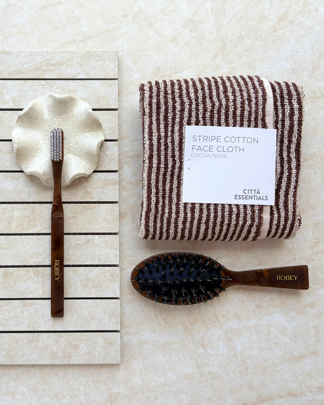 Taj Mahal Linea porcelain mosaic tiles arranged in horizontal strips, styled with a burgundy-striped face cloth and wooden grooming brushes.