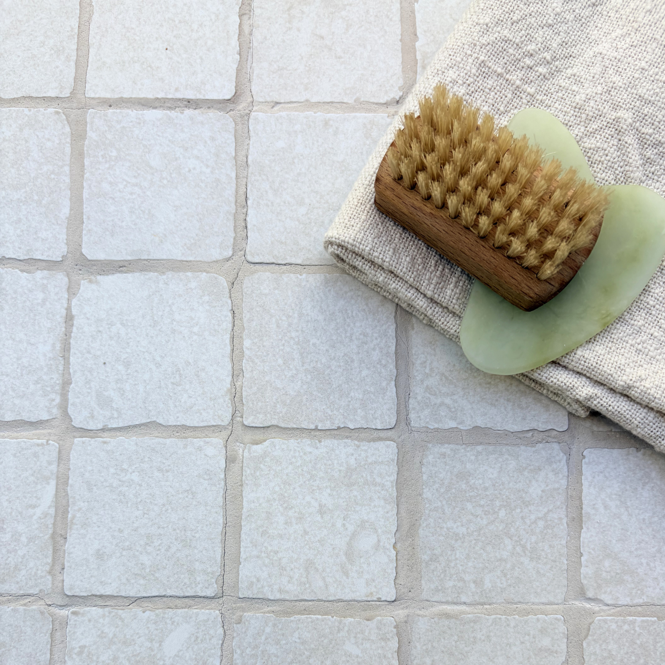 Limestone Tumbled Bianco off-white porcelain mosaic tiles styled with a wooden body brush, pale green soap and folded natural linen fabric.