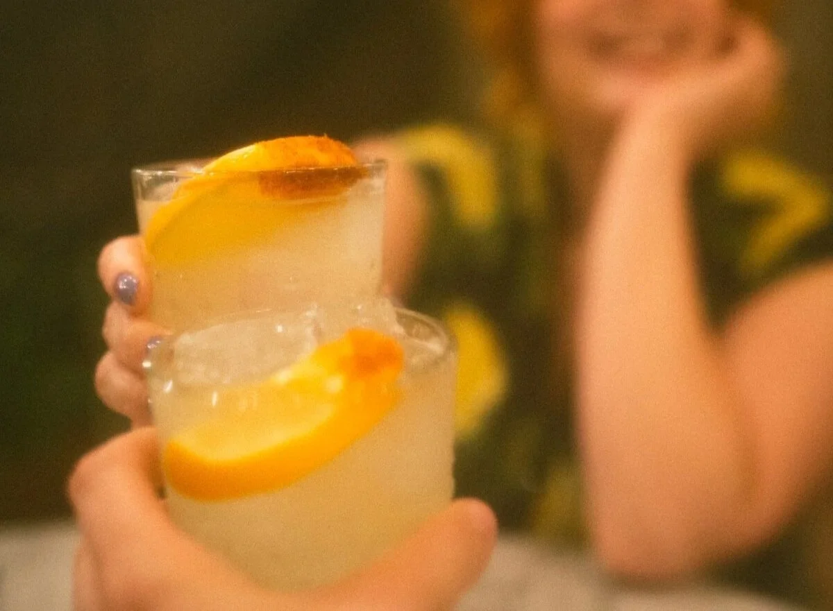 A person holding two glasses of a lemon drink with lemon slices inside.