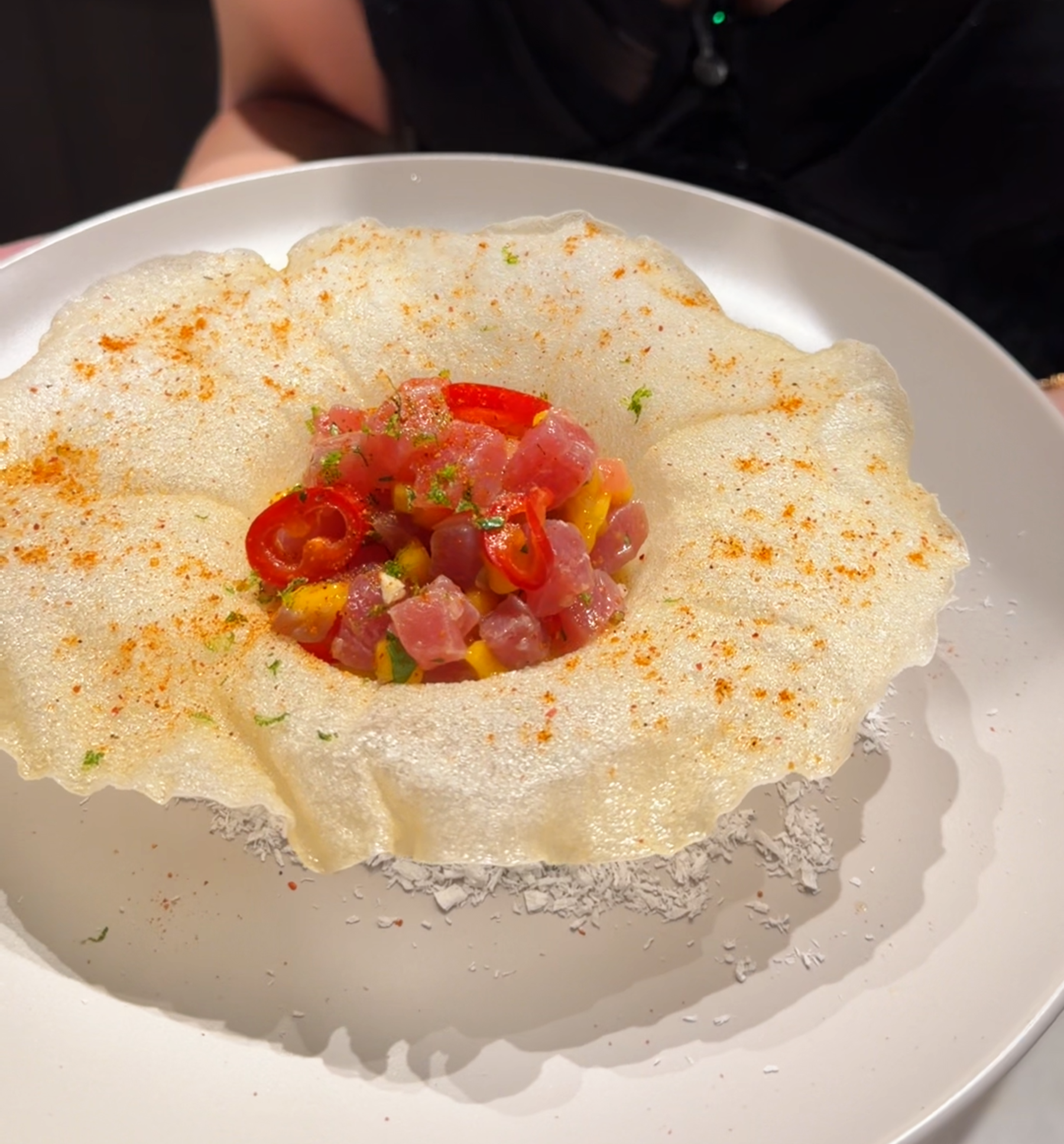 tuna tartare with mango and red chilies served in a crispy fried rice-paper boat dusted with gochugaru, on a white plate