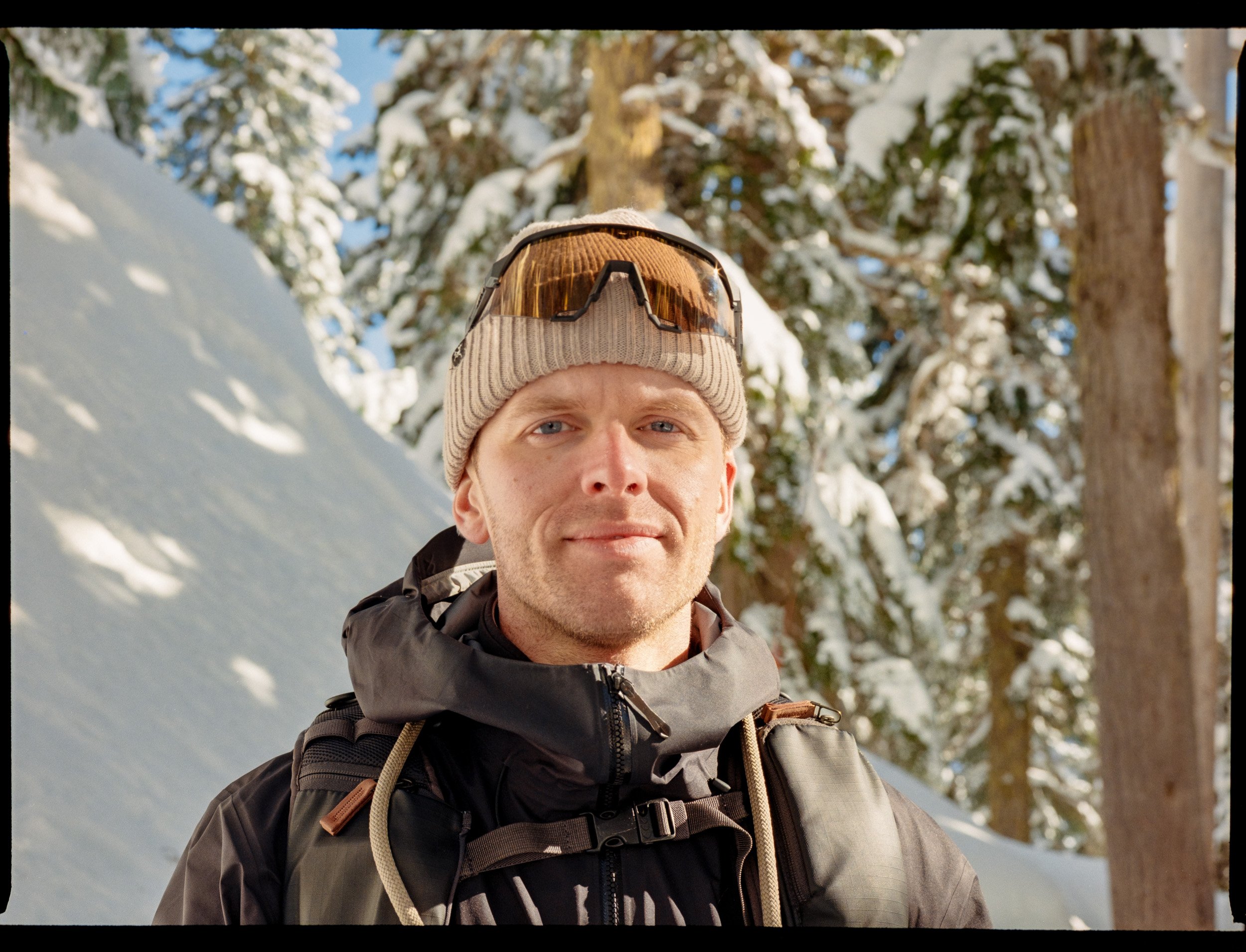 Man wearing a beanie and goggles on snowy forest background