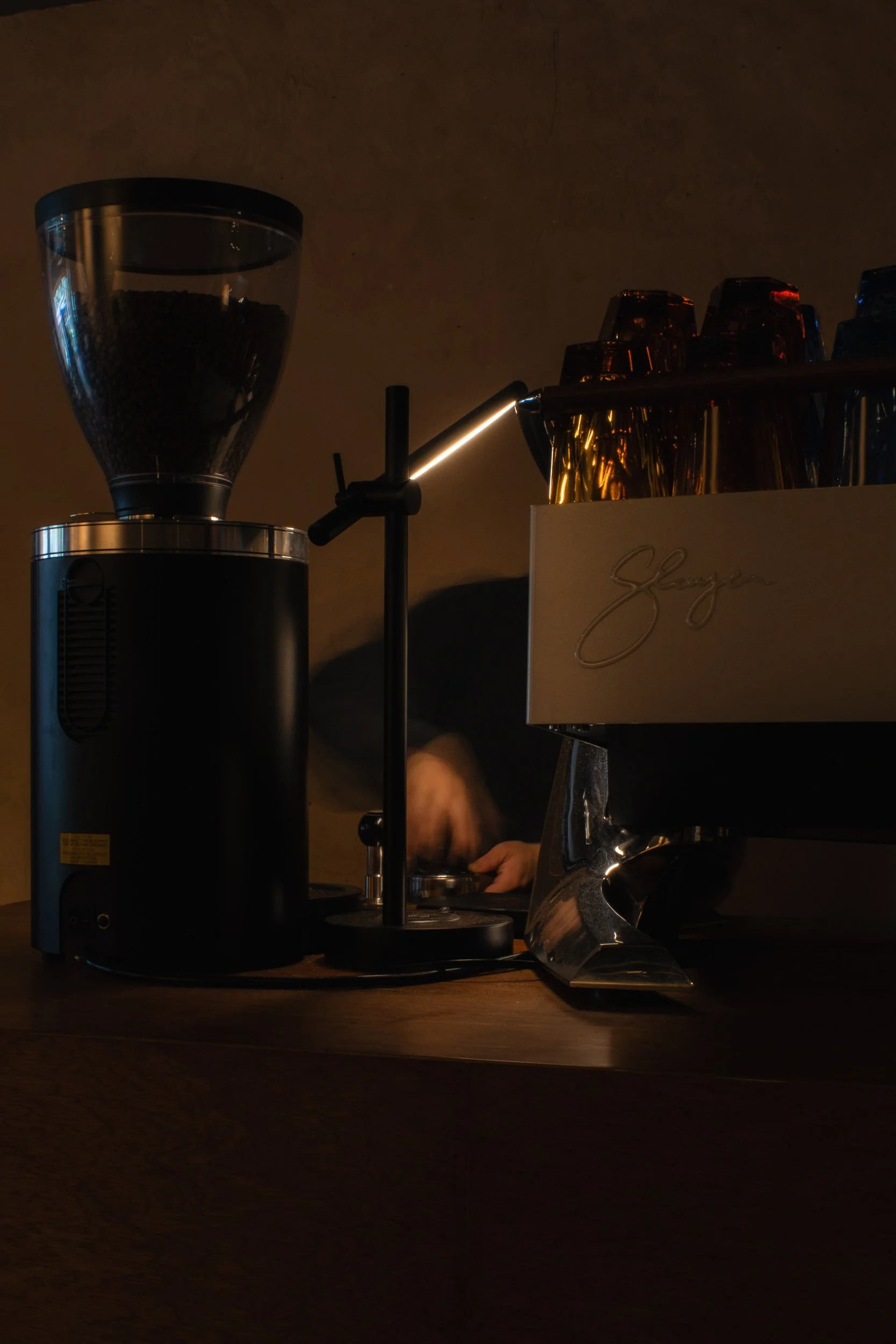 A coffee grinder and coffee cups on a counter in a dimly lit setting.