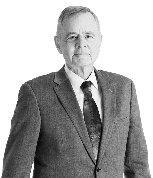 Older man in a suit and tie standing against a plain background.