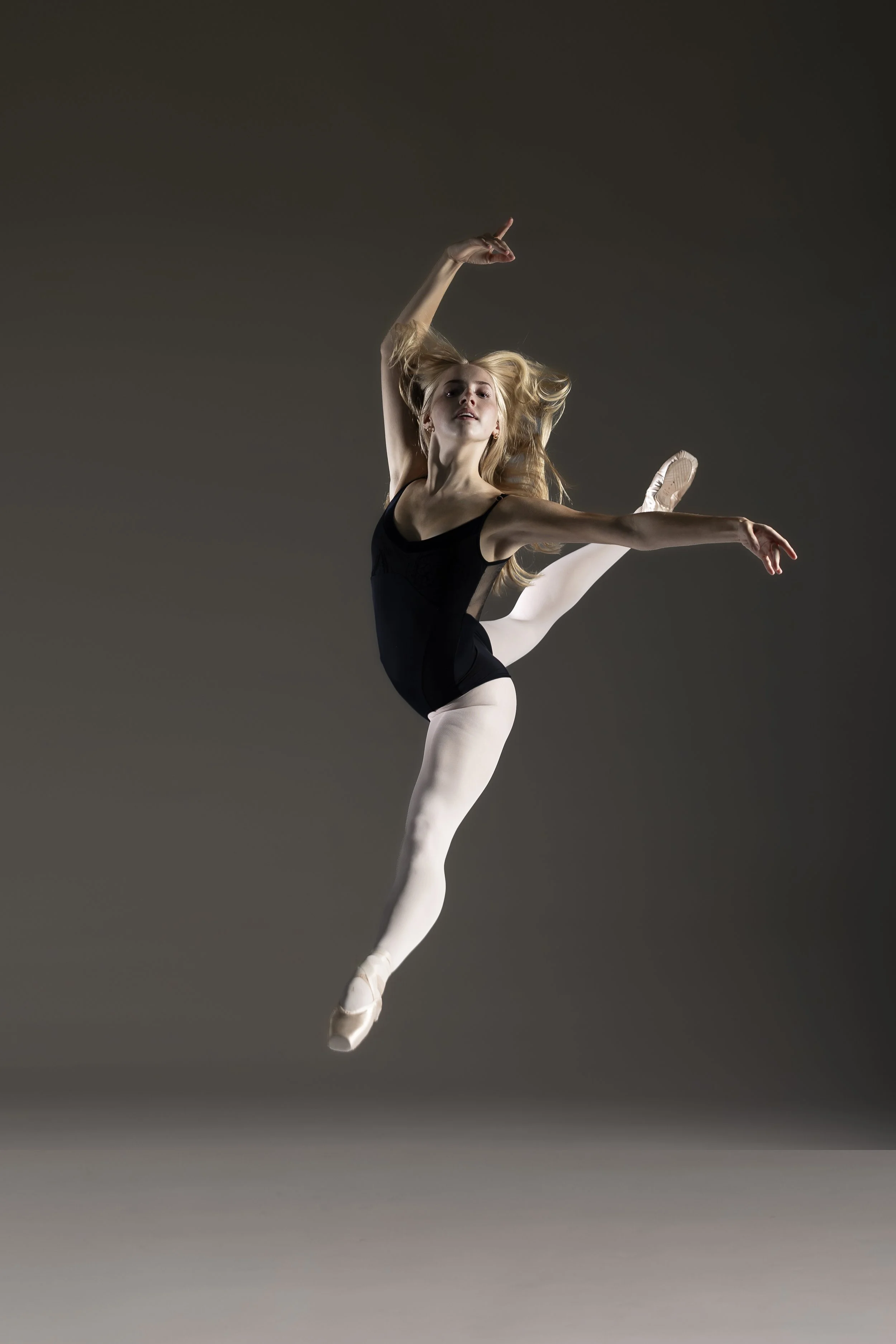 Ballet dancers practicing in a dance studio, wearing black leotards and pink tights, with their arms raised and poised.