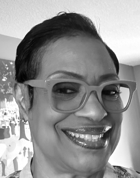 A woman with short dark hair and glasses smiling in a grayscale photo.