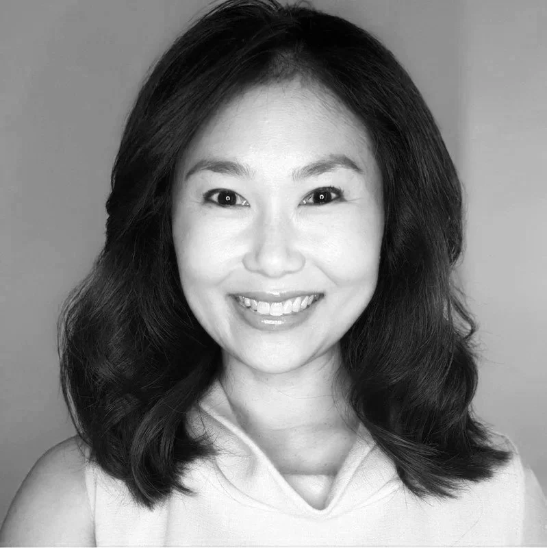 Black and white portrait of a smiling woman with shoulder-length wavy hair wearing a sleeveless top.