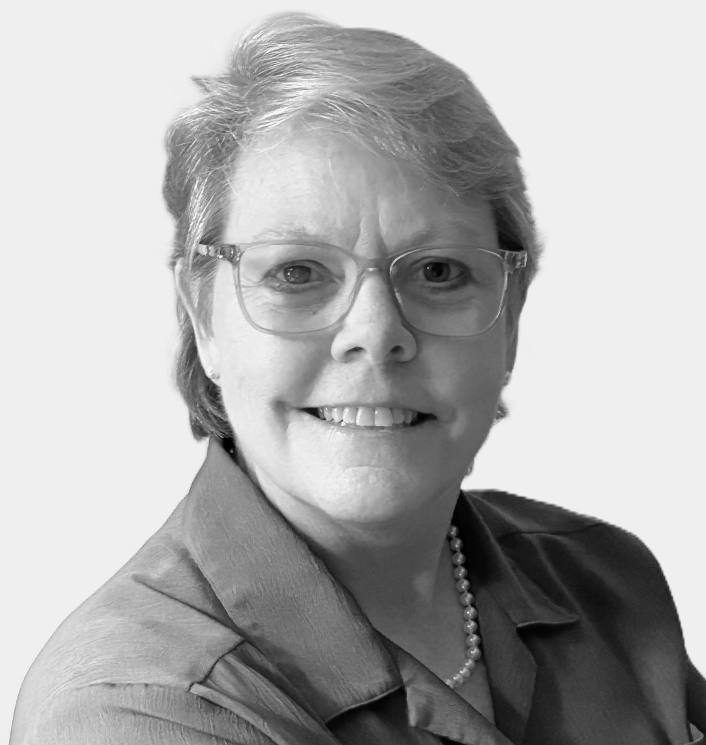 A black-and-white portrait of a smiling middle-aged woman with short hair, wearing glasses, a pearl necklace, and a collared shirt.