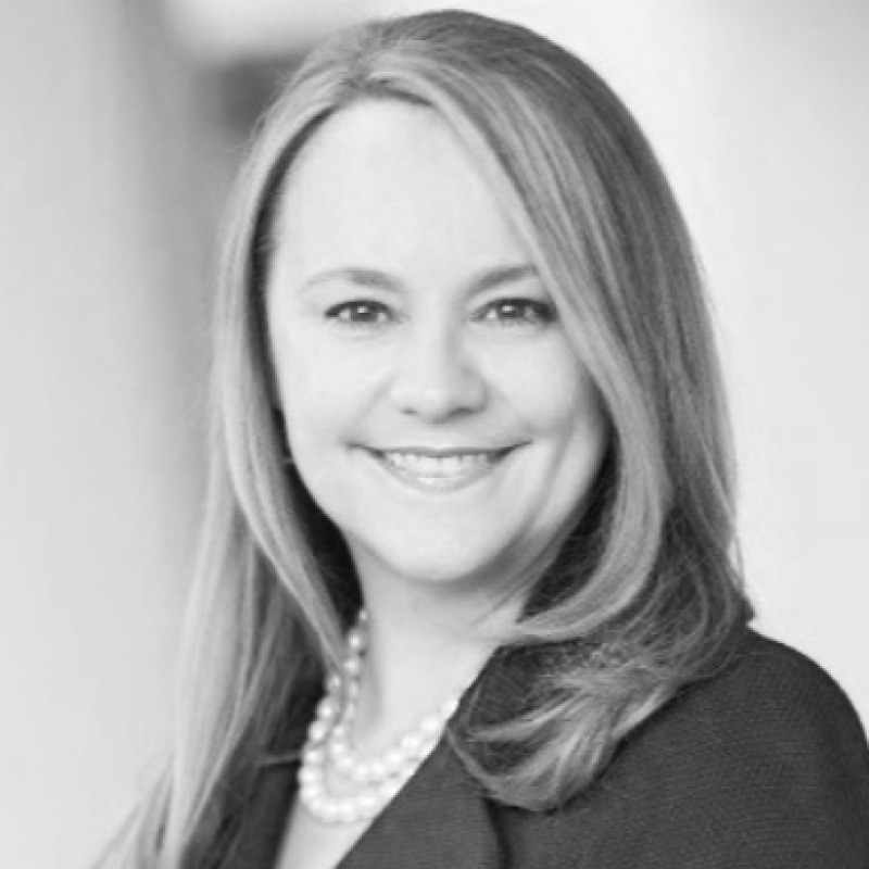Black and white photo of a smiling woman with shoulder-length hair, wearing a pearl necklace and a dark blazer.