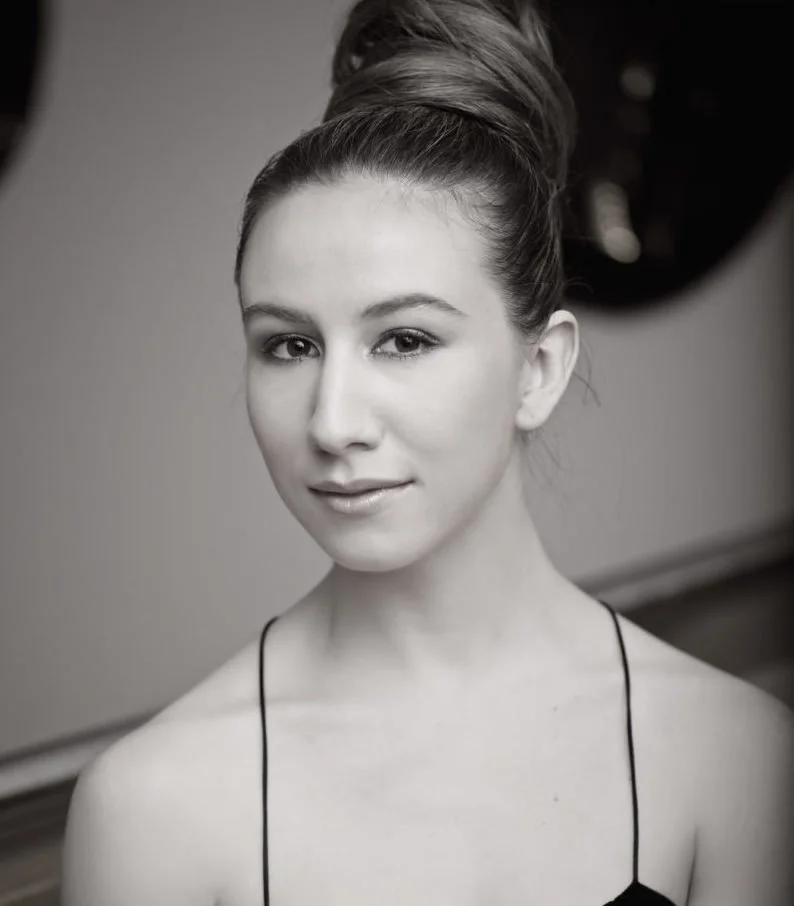 A young woman with her hair in a high bun, smiling slightly, in black and white portrait.