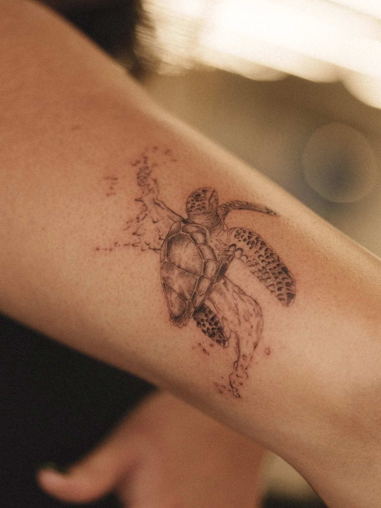 A micro realism tattoo of a sea turtle with a splash of water in the background. It’s got soft shaking, looks realistic and highly detailed