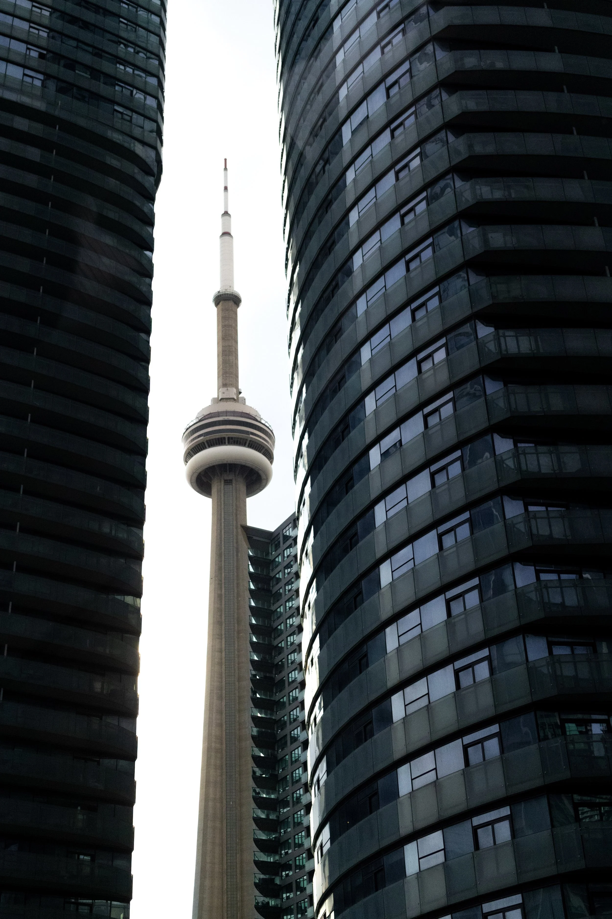 Tall TV tower between two modern high-rise buildings with glass facades.