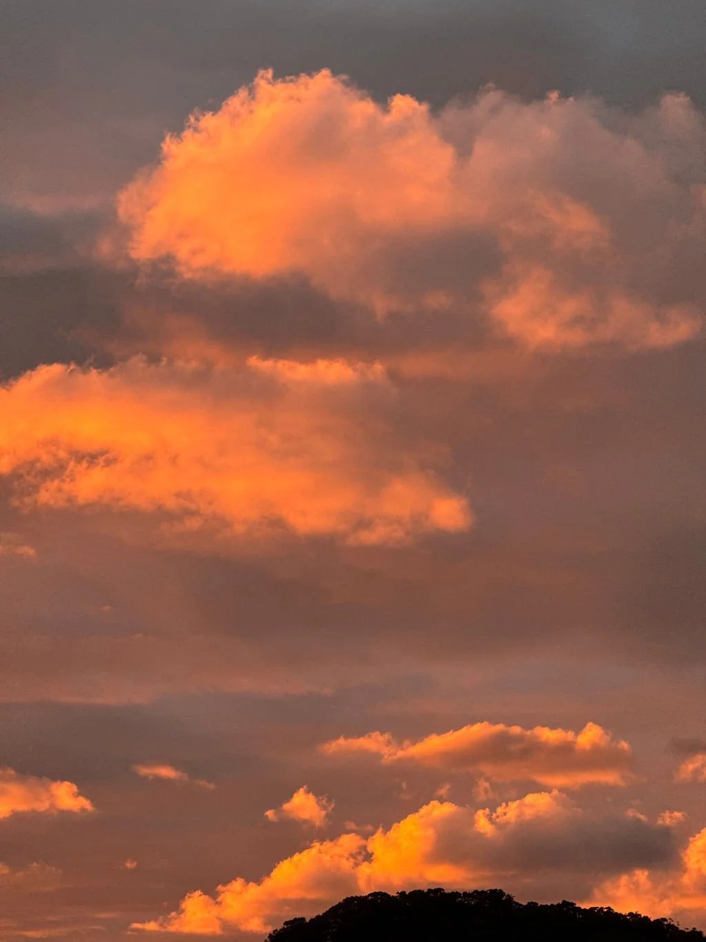 Orange-pink clouds at sunset over a dark silhouette of a hill or mountain range.