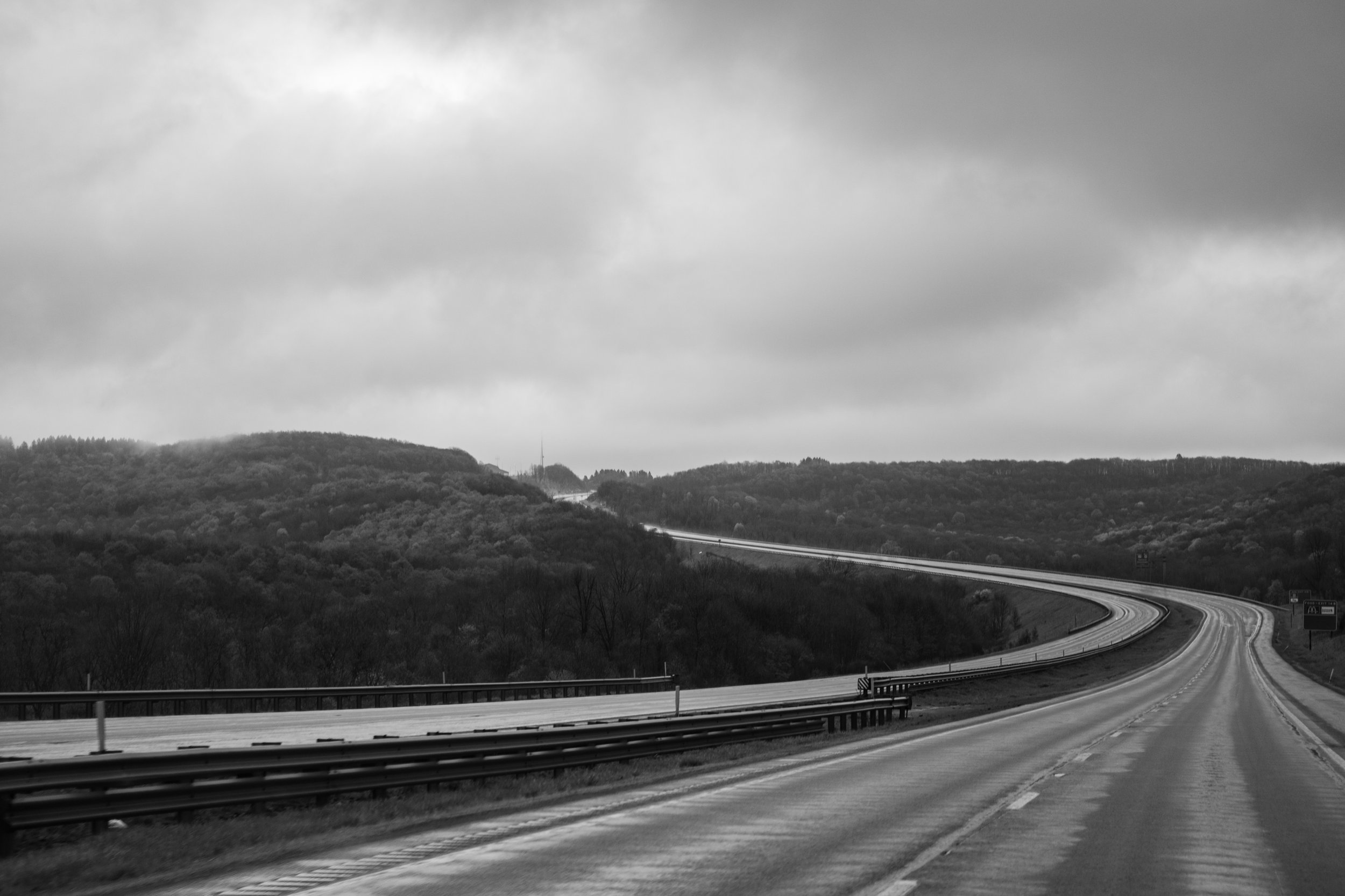 A winding highway through a hilly landscape with trees and clouds overhead.