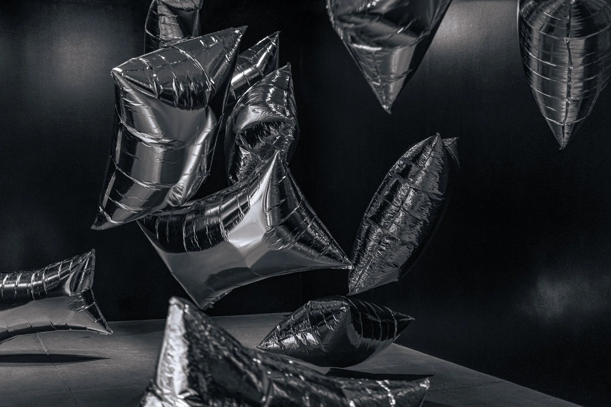 Multiple black silver foil balloons in various shapes, floating against a black background.