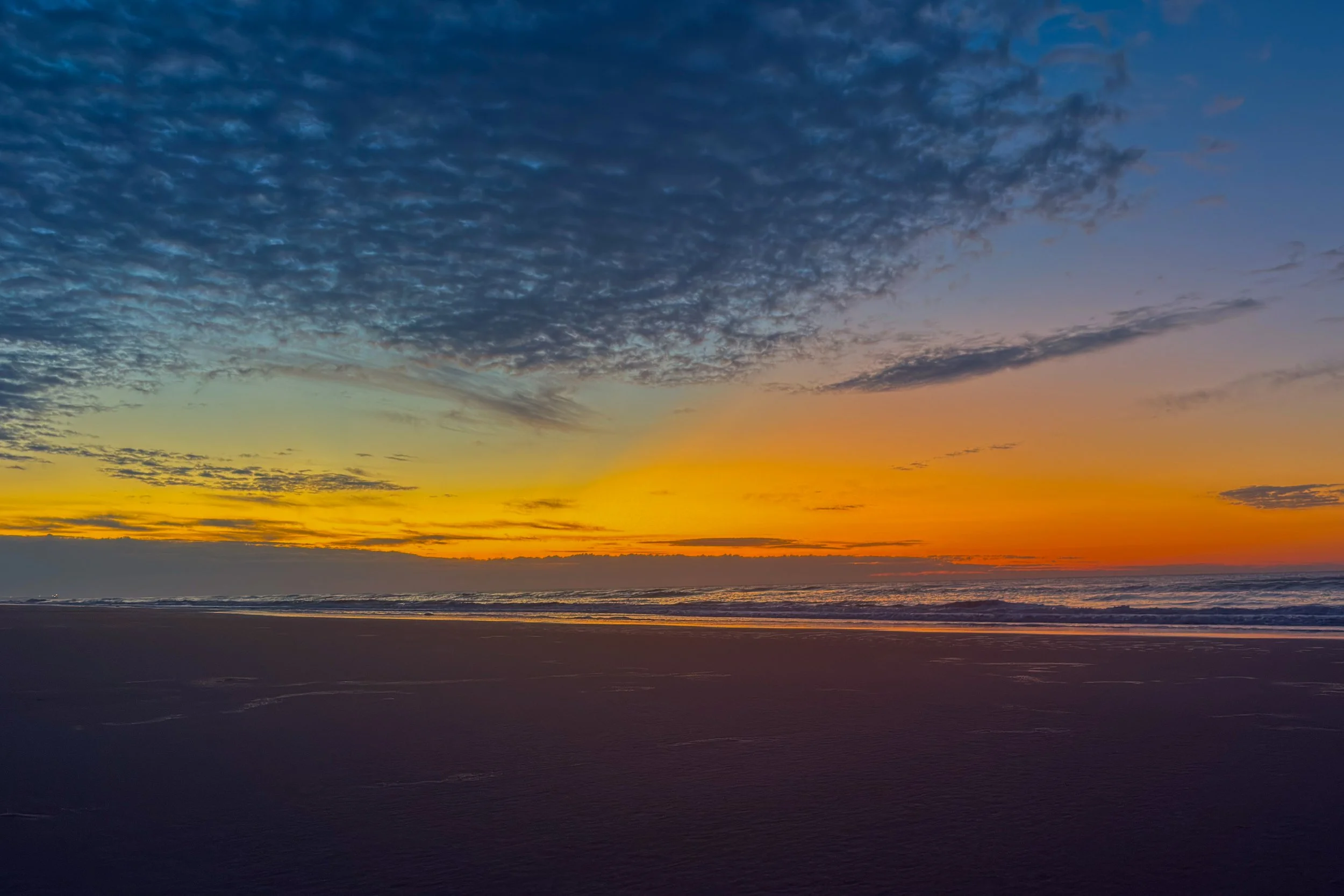 Sunset over the ocean with a colorful sky and scattered clouds.