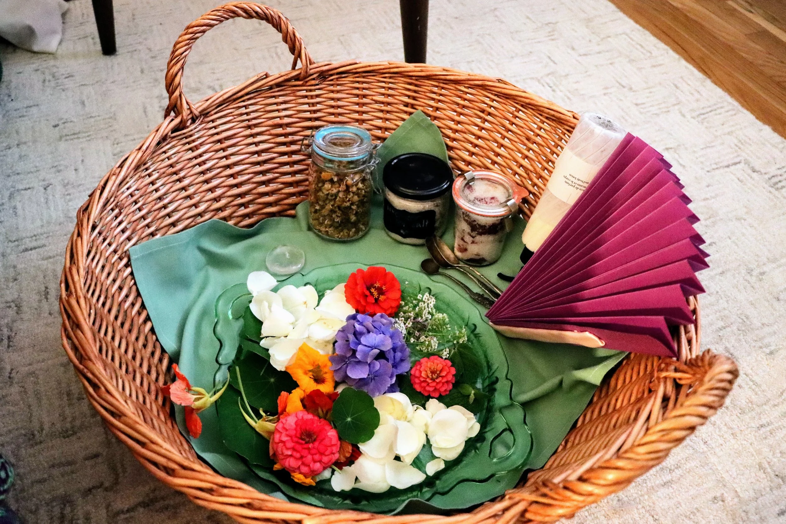Basket of components for the ceremonial foot bath, including fresh flower petals, dried lavender and chamomile, homemade rose and lavender epsom salts, her favorite lotion and a fan to pamper mama.