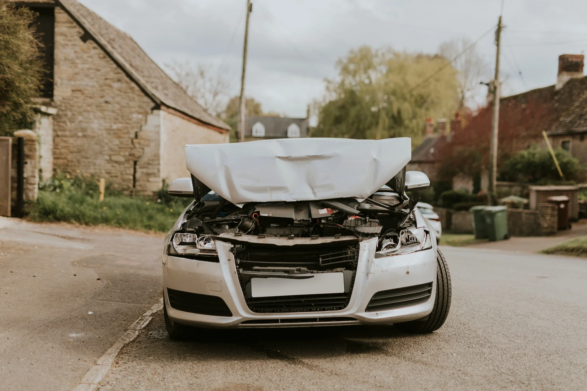 A white car with front-end damage and a deployed airbag on a residential street.