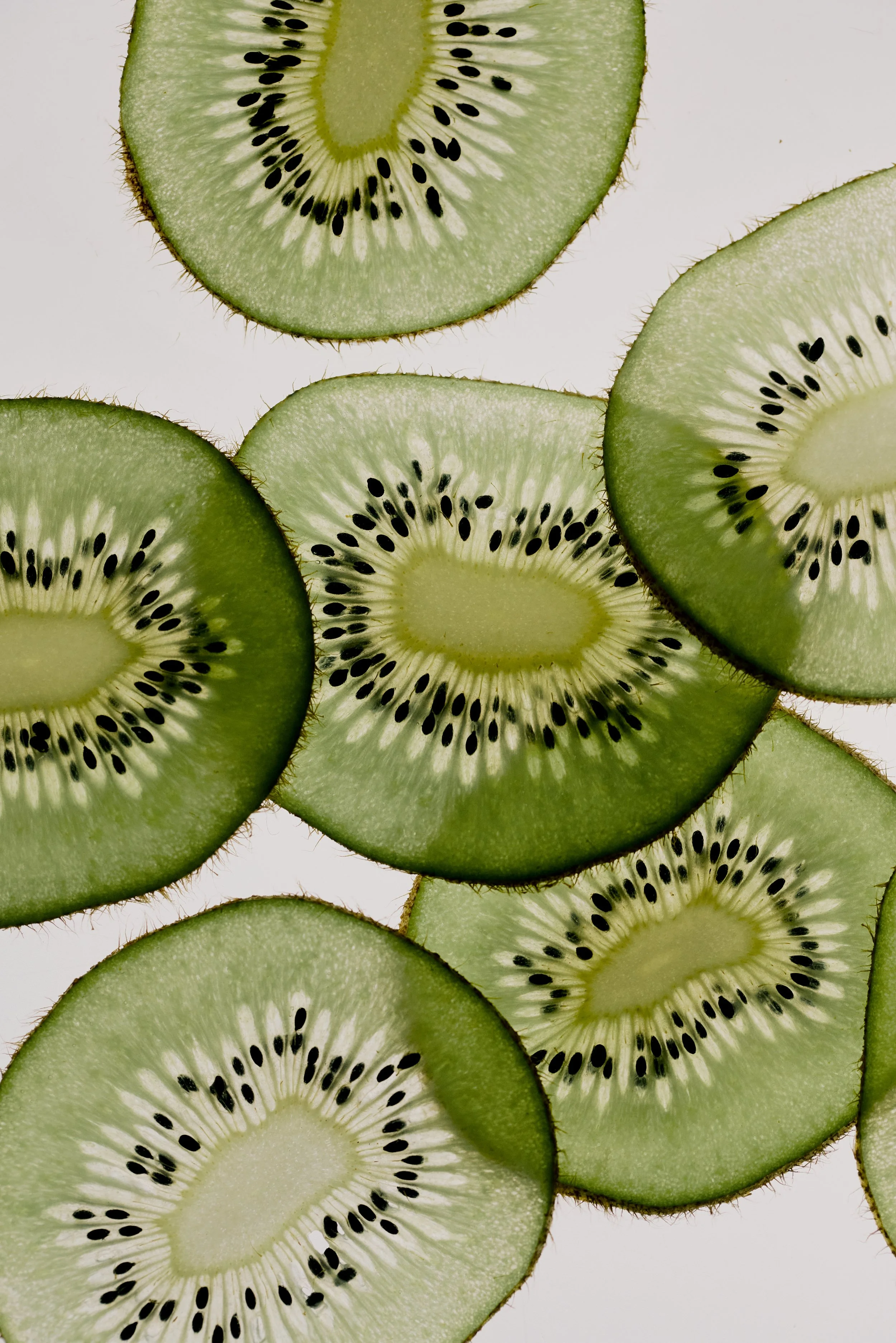 Close-up of overlapping kiwi slices with visible seeds against a white background.