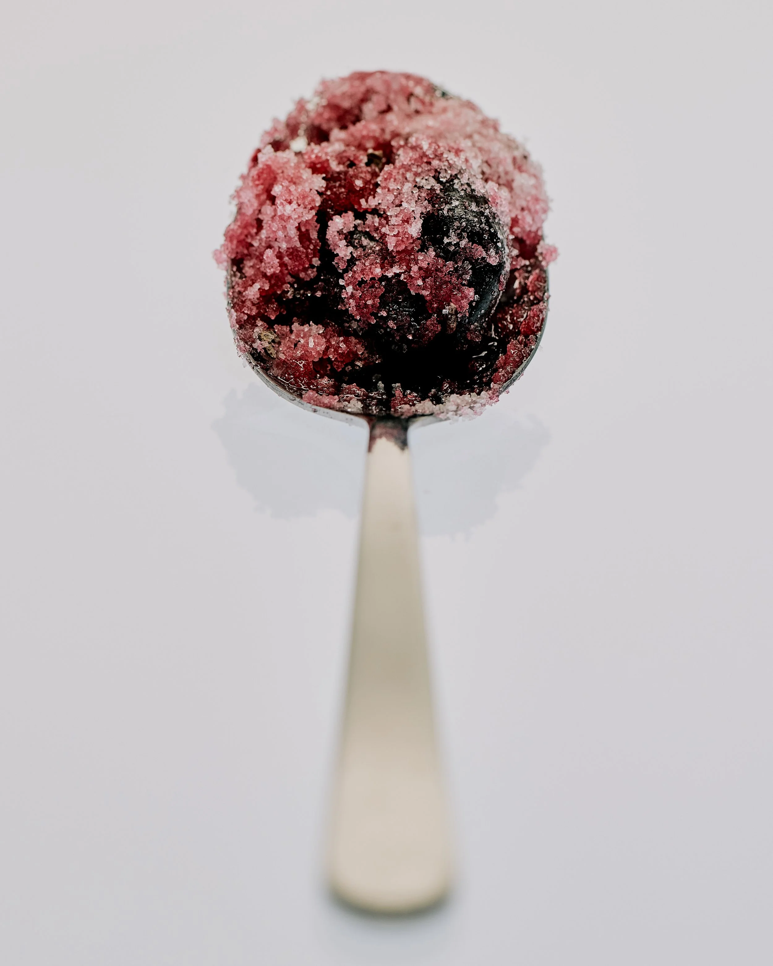 A spoon filled with dark berries coated in sugar on a light background.