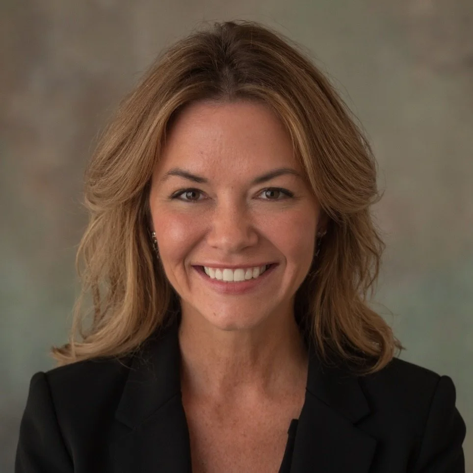 Smiling woman with curly hair, glasses, hoop earrings, layered necklaces, and a striped shirt.