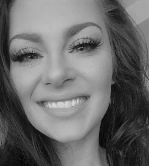 Close-up of a woman smiling, wearing makeup with long eyelashes, in black and white.