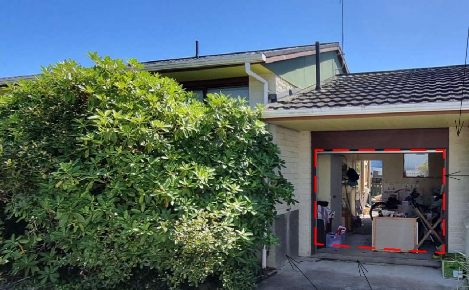 A partially open garage with visible tools and furniture inside, next to a large green bush, under a clear blue sky.