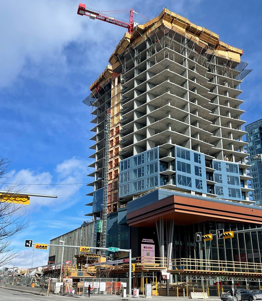 Construction site with a high-rise building under construction and a red crane at the top, with scaffolding, glass windows, and a partially completed structure.