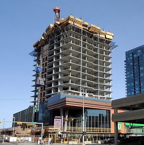 Under construction high-rise building with a crane on top and scaffolding around the edges in an urban area.