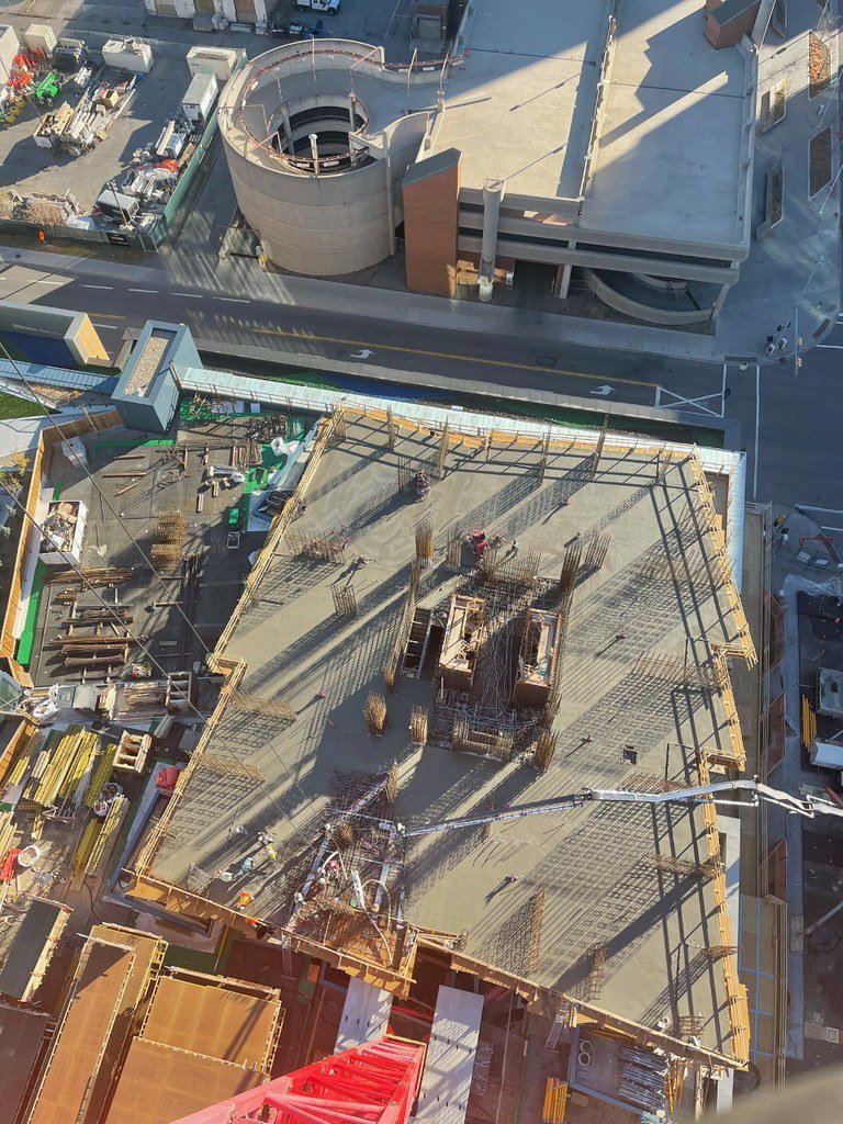Aerial view of a building under construction with concrete slab and rebar framework, surrounded by construction materials and equipment.