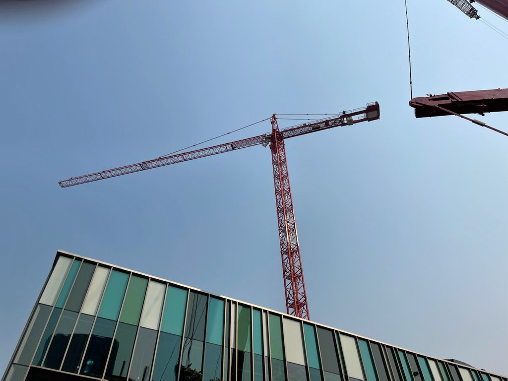 Construction crane towering over a glass building under a clear blue sky.