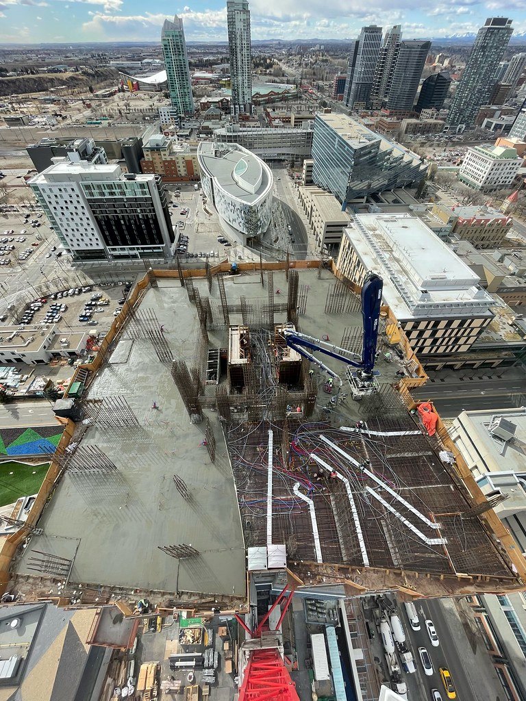 View from a high-rise building showing construction site with concrete and rebar, surrounded by various modern buildings in a cityscape.