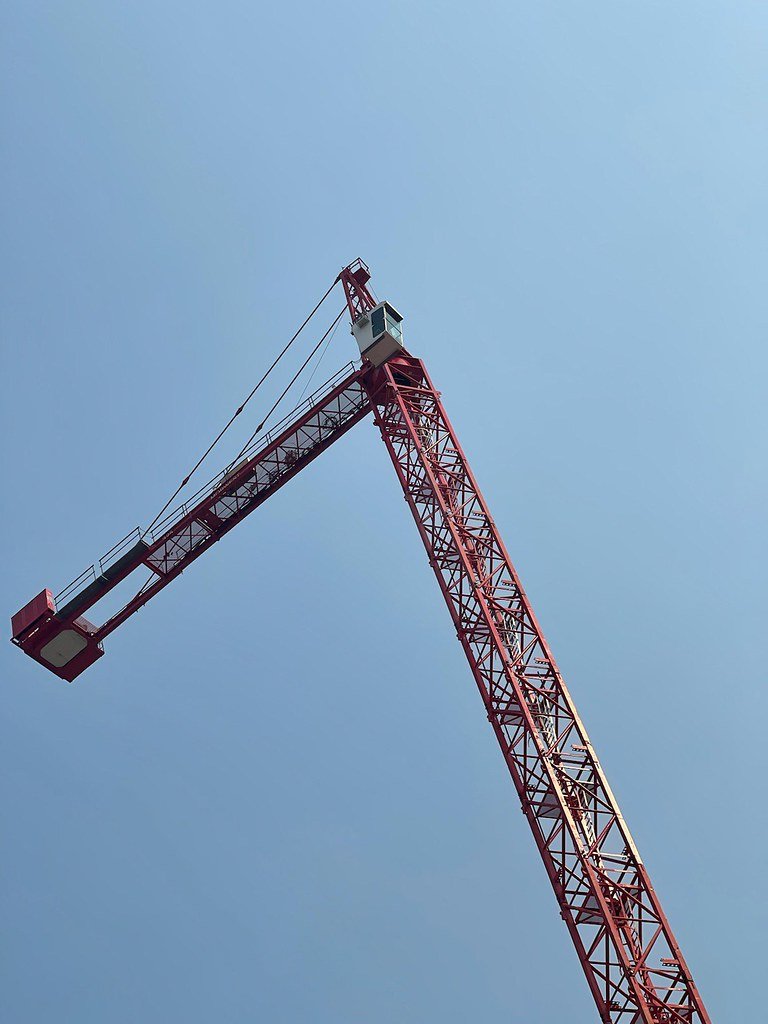 A tall red construction crane reaching into a clear blue sky.