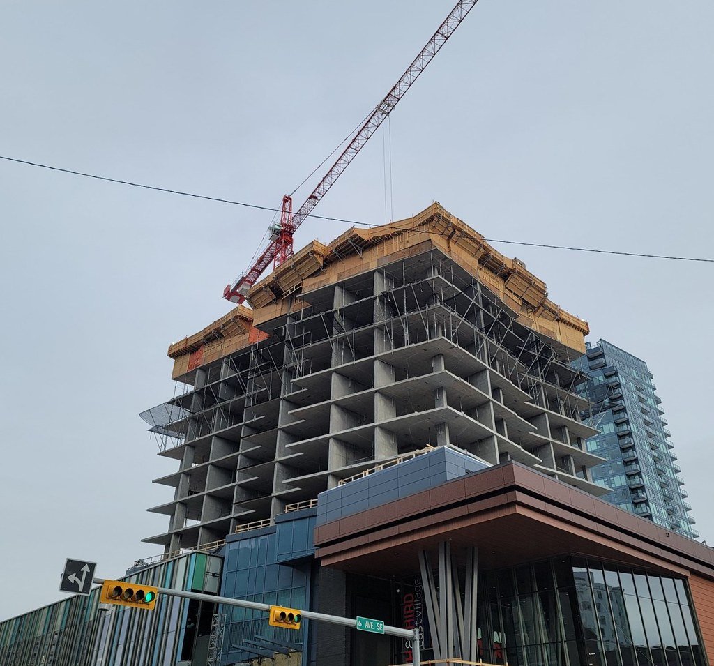 Construction site with a high-rise building under construction, scaffolding around the middle, and a tower crane above it.