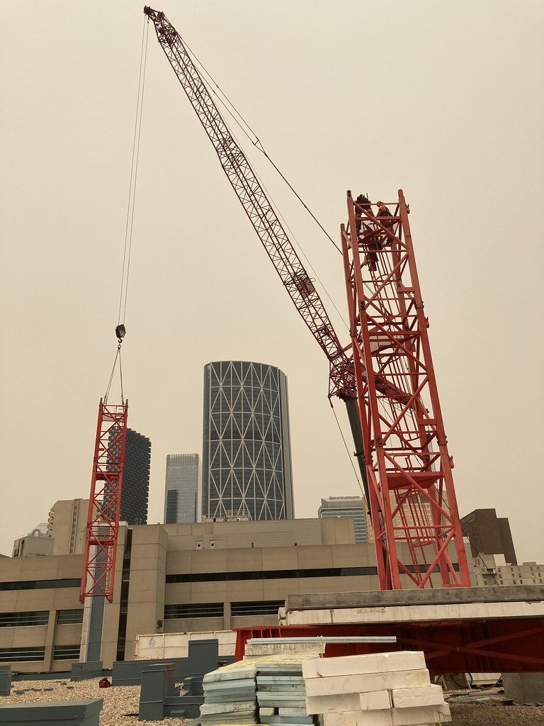 Construction crane on a rooftop with city skyscrapers in the background.