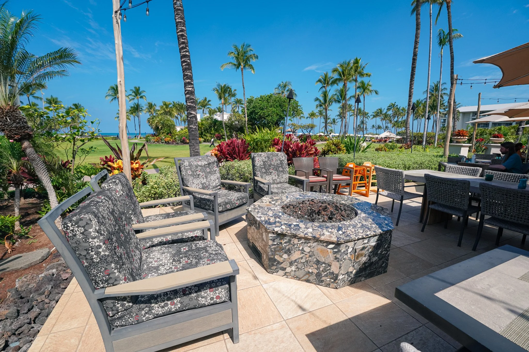 Daytime lounge area outside Orchid Court with a stone fire pit, seating, and ocean views