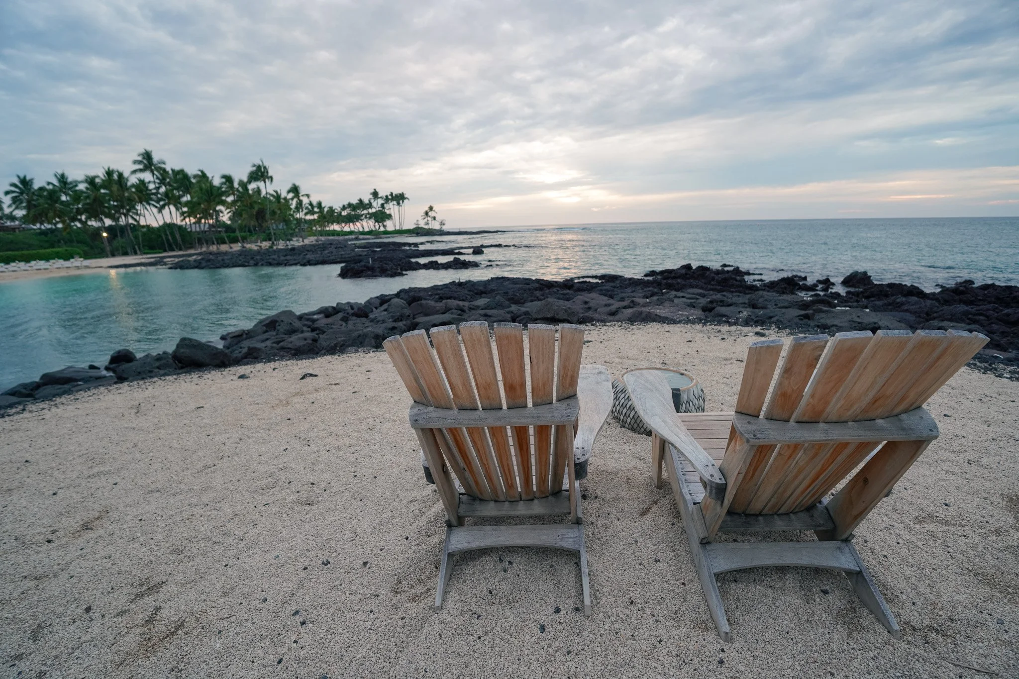 Two wooden Adirondack chairs overlooking the Kohala Coast at golden hour