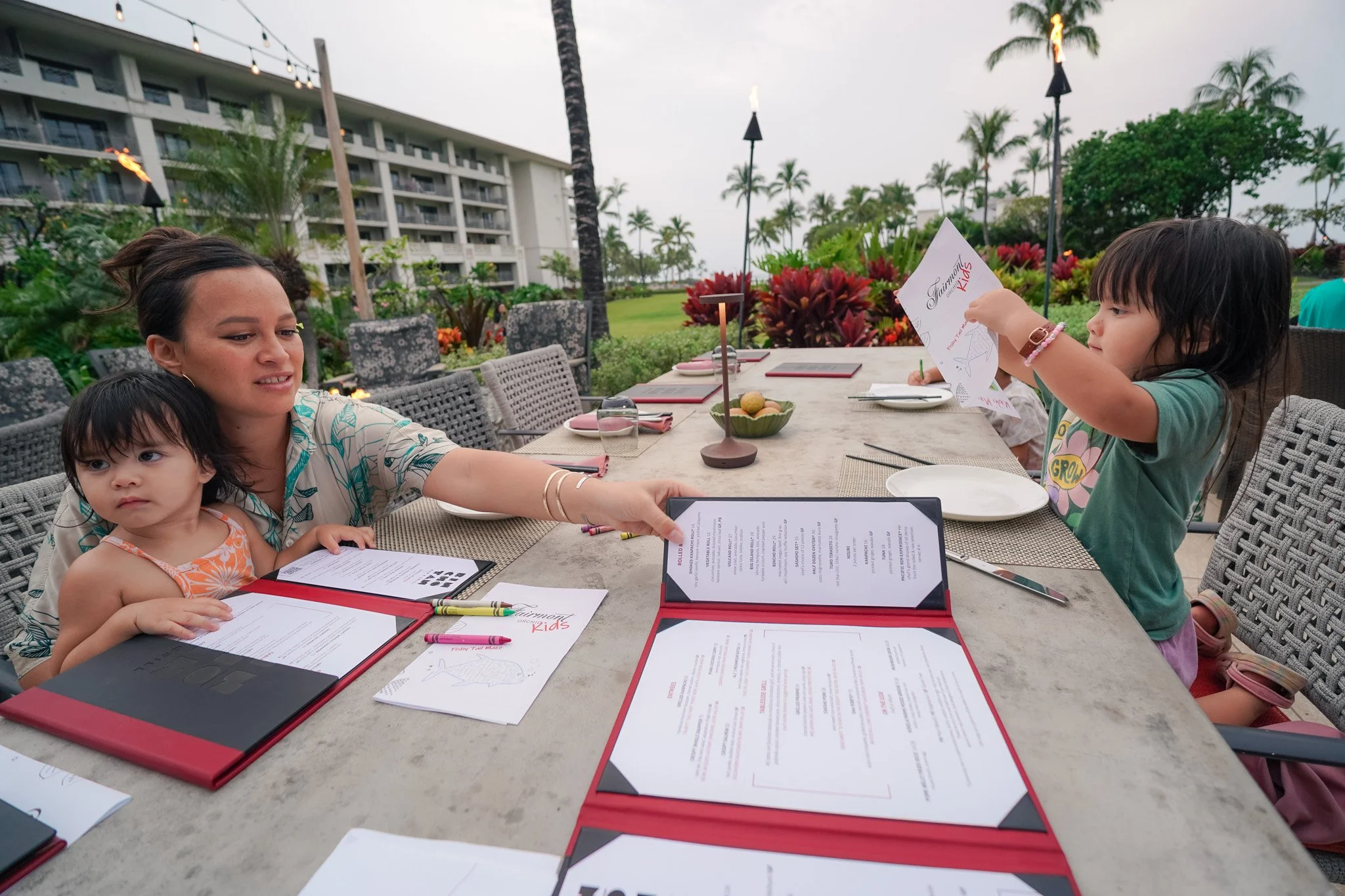 Our family seated at Binchotan with the Fairmont Kids menus and tiki torches lit behind us