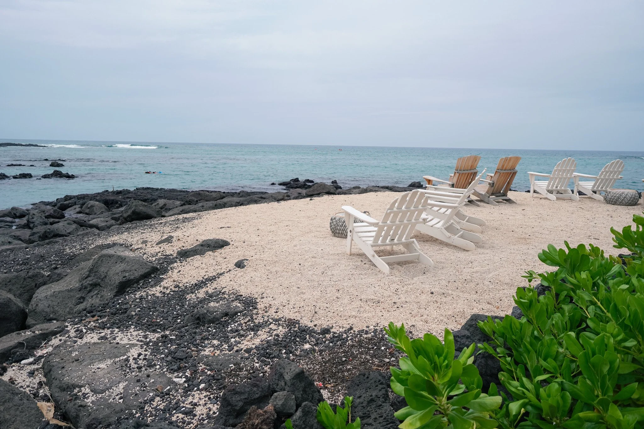 Black sand beach area at the Fairmont Orchid with white Adirondack chairs facing the ocean