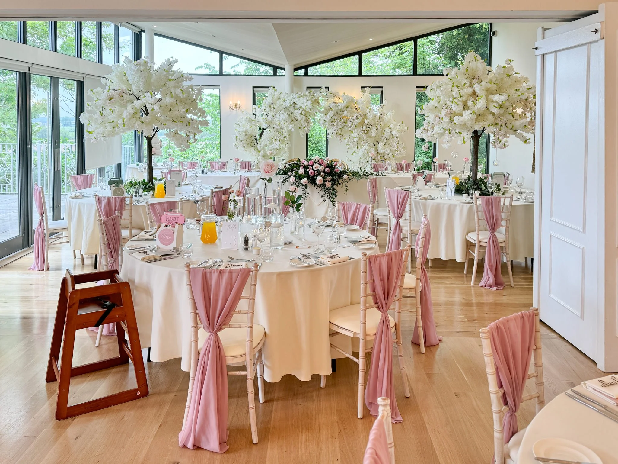 a photograph showing pink chair drapes, ivory blossom trees and pink fresh florals. Ivory and pink wedding styling at West Tower.