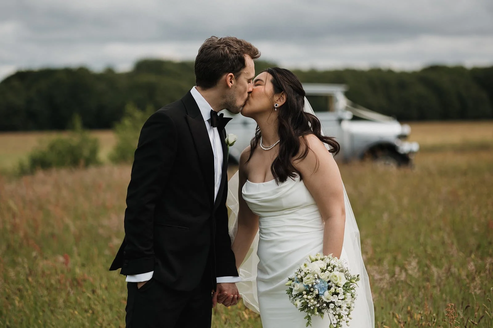 Meols Hall Wedding Photography showing the couple kissing in the fields with the wedding car in the background.