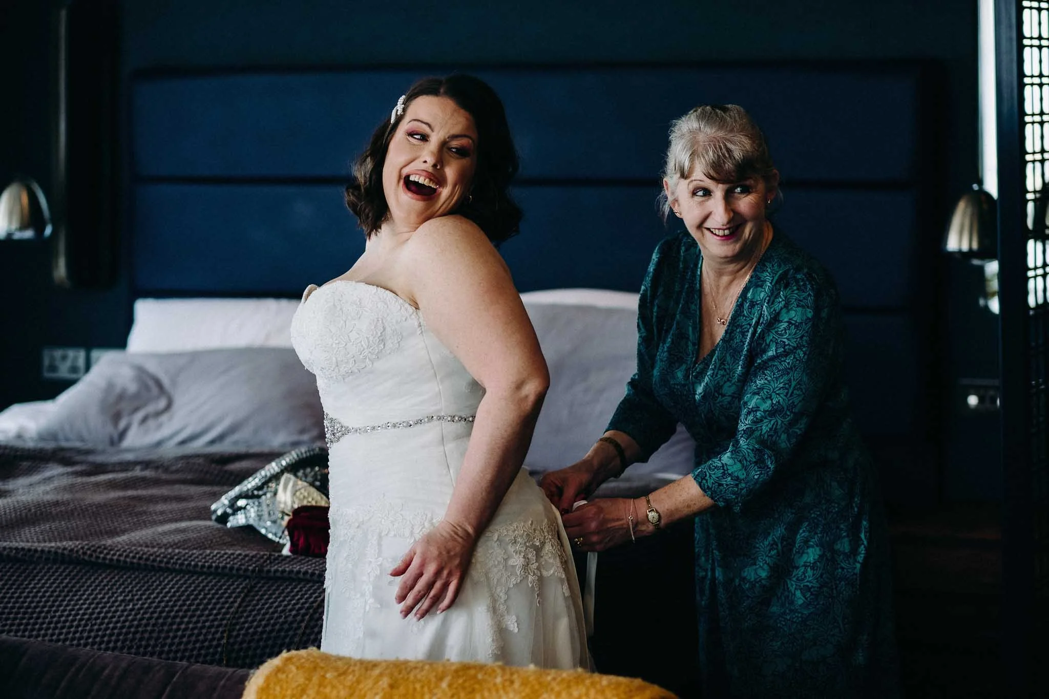 a bride laughing with her mum as she puts on her wedding dress in a Liverpool wedding venue.