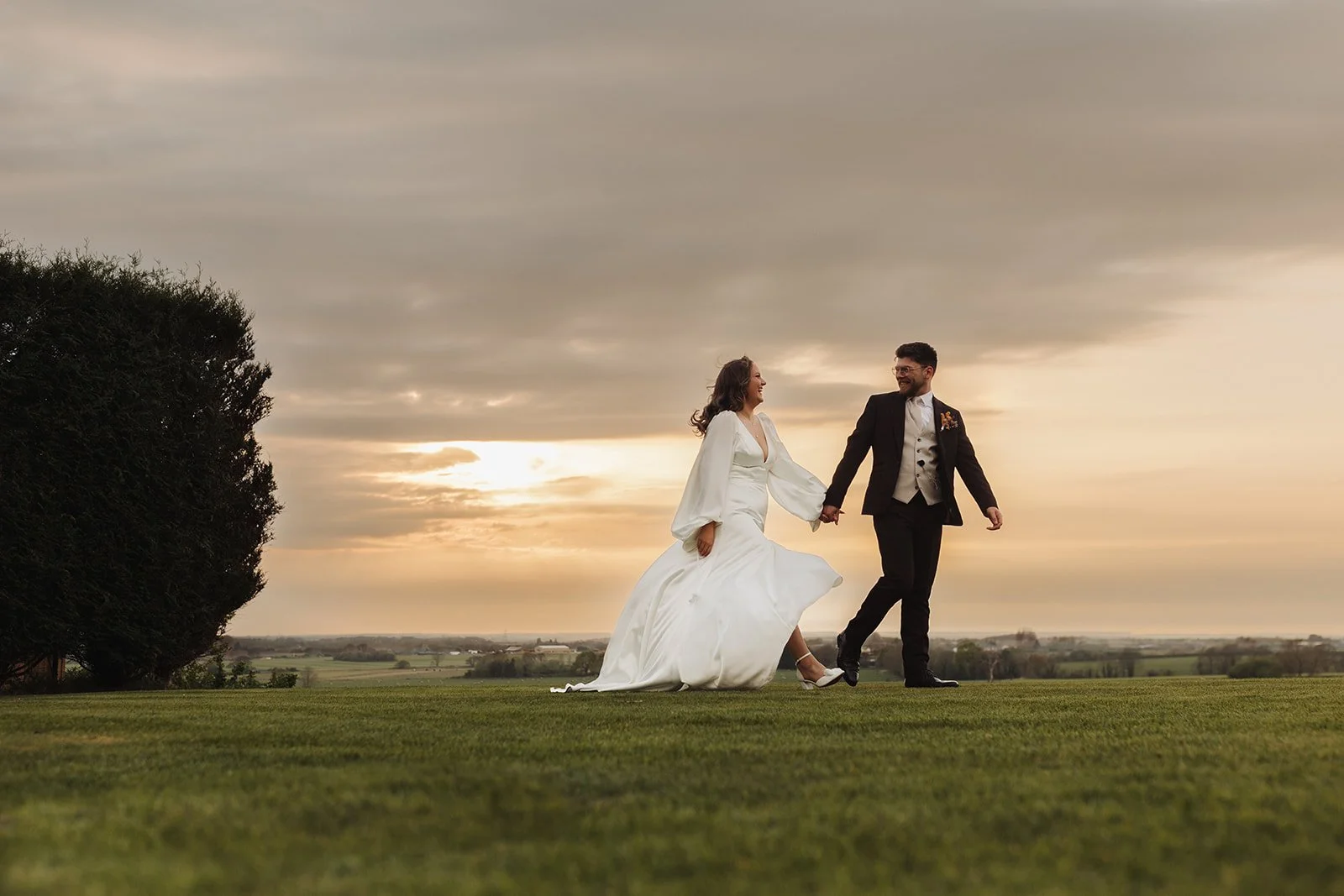 a beautiful wedding photograph of the bride and groom walking across the lawn at West Tower during golden hour.