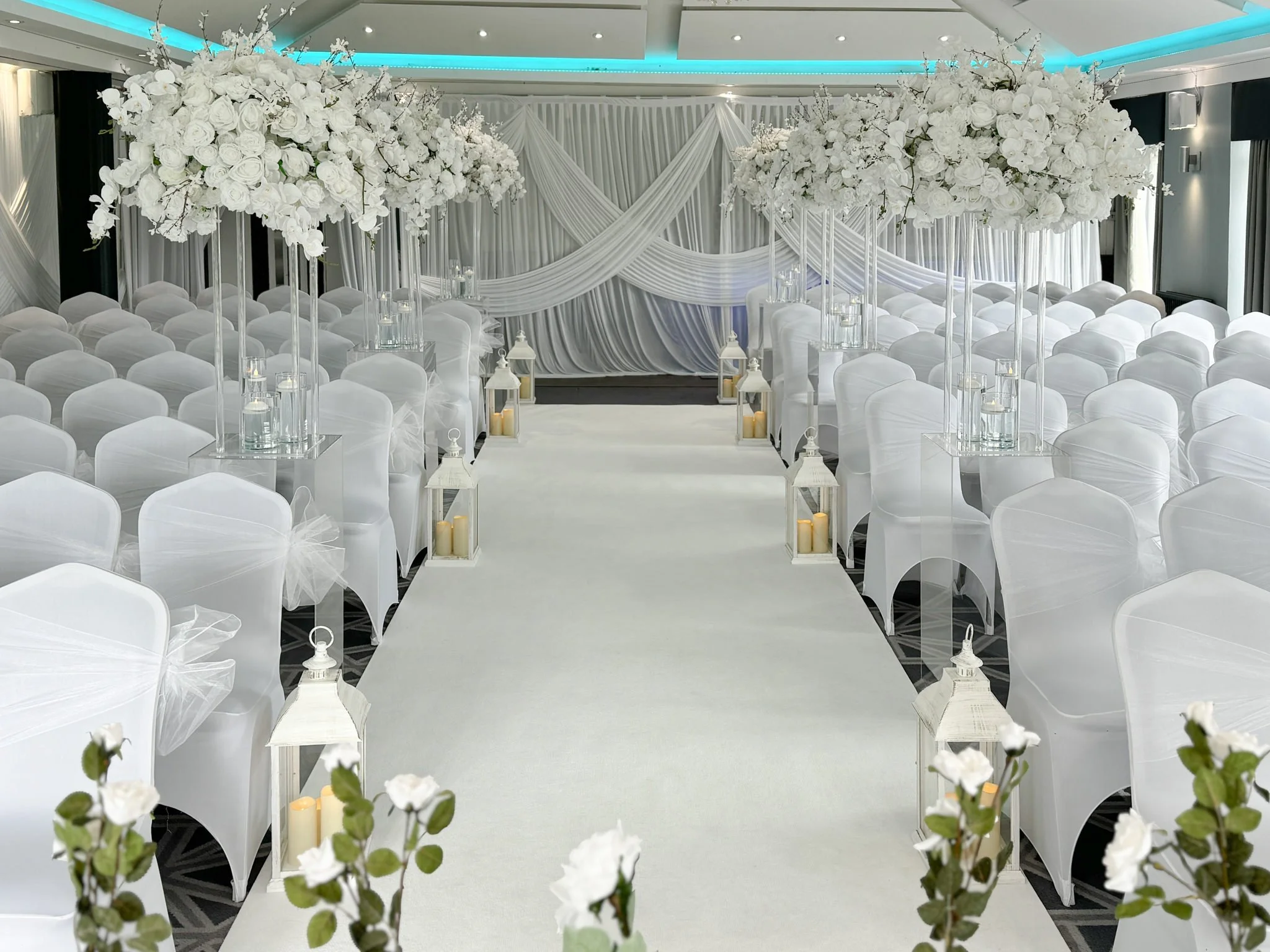Wedding aisle at Formby Hall Golf Resort and Spa dressed in white florals, lanterns and white room draping.